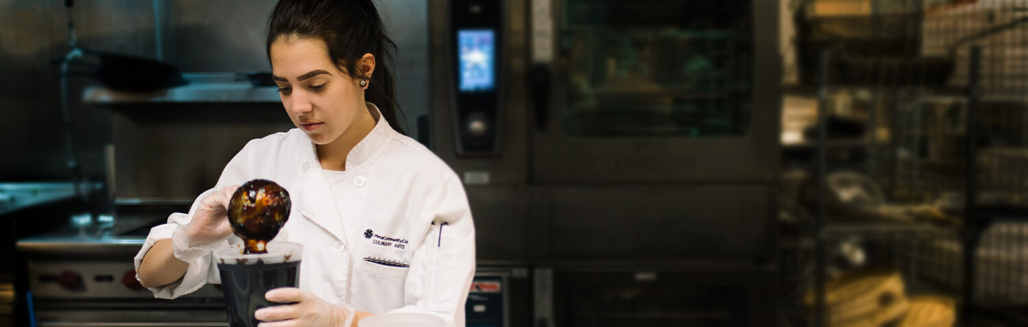 A cooks stand pouring a sauce in a container in a kitchen at pima