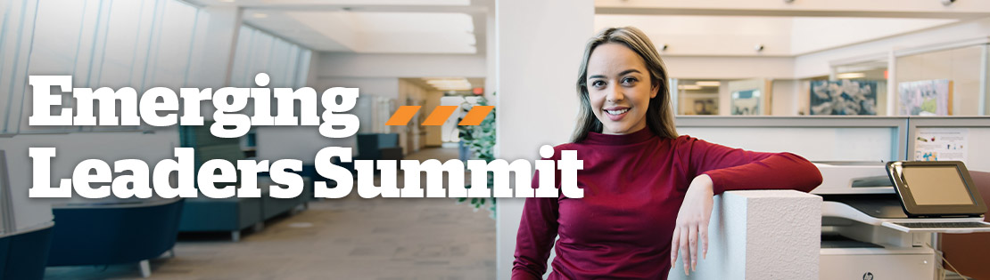 A student smiles at the camera standing in an office space. Associated text says "Emerging Leaders Summit"