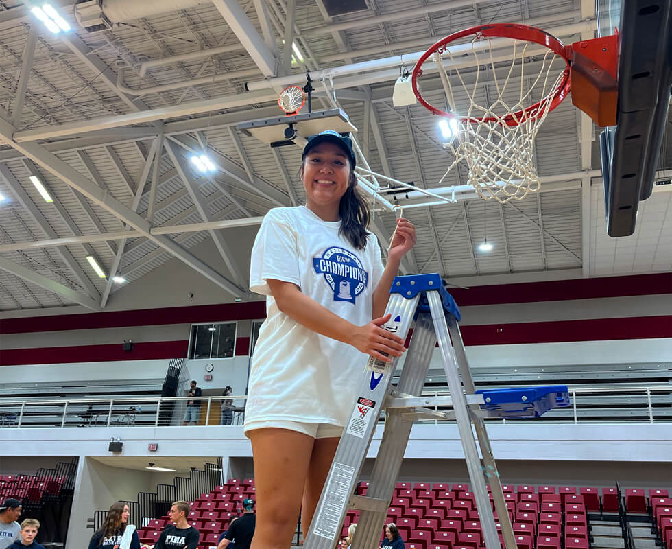 Melicia Nelson standing on a ladder next to a basketball net.