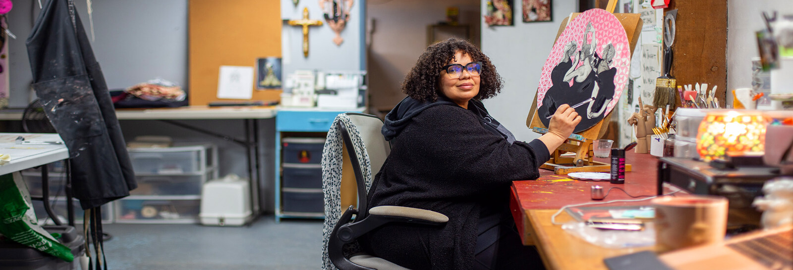 Lizz Denneau works in her studio smiling at the camera