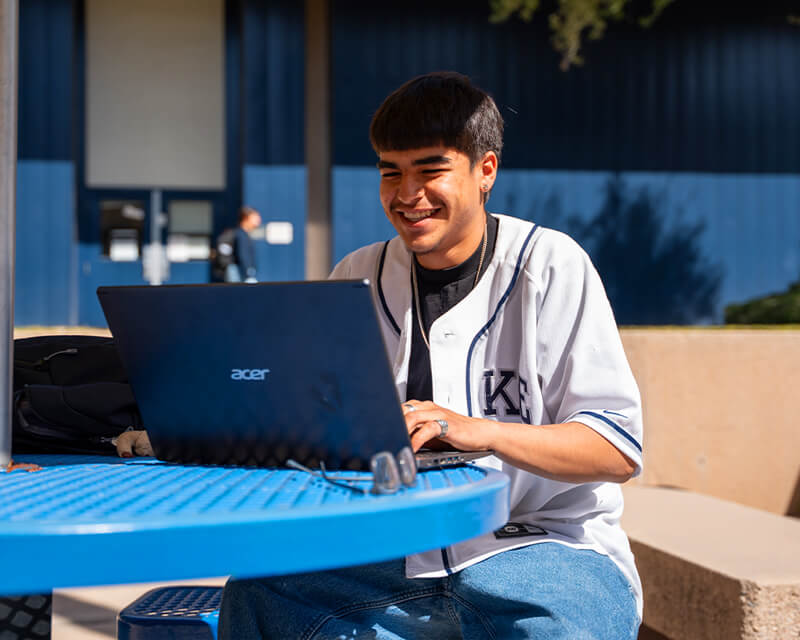 Students sits at a table at West Campus on a laptop.