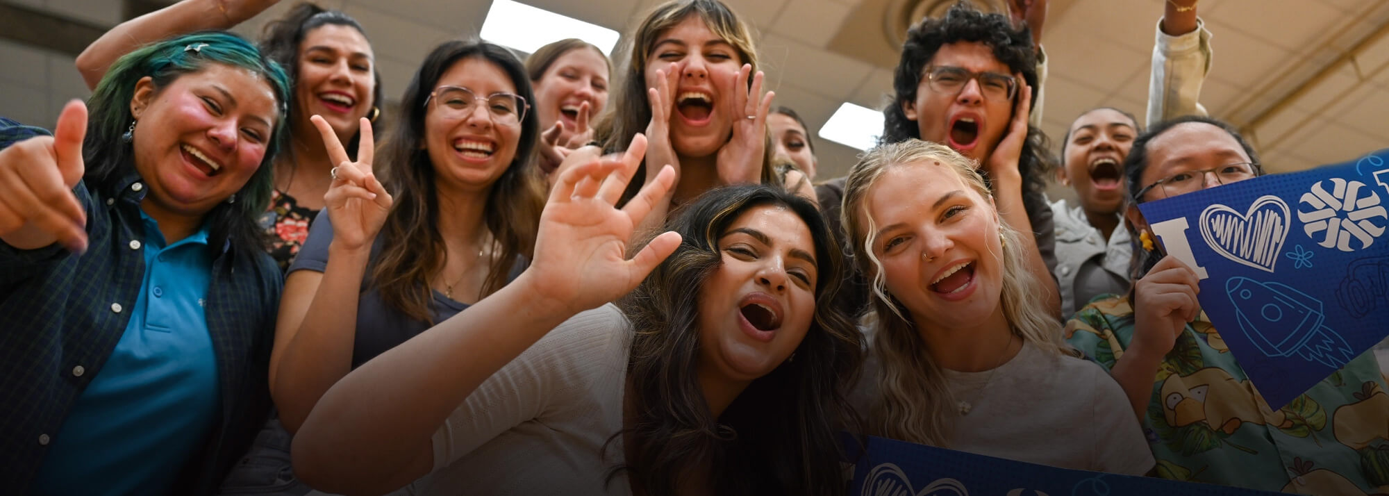 A group of students cheering and holding a Pima Community College banner.