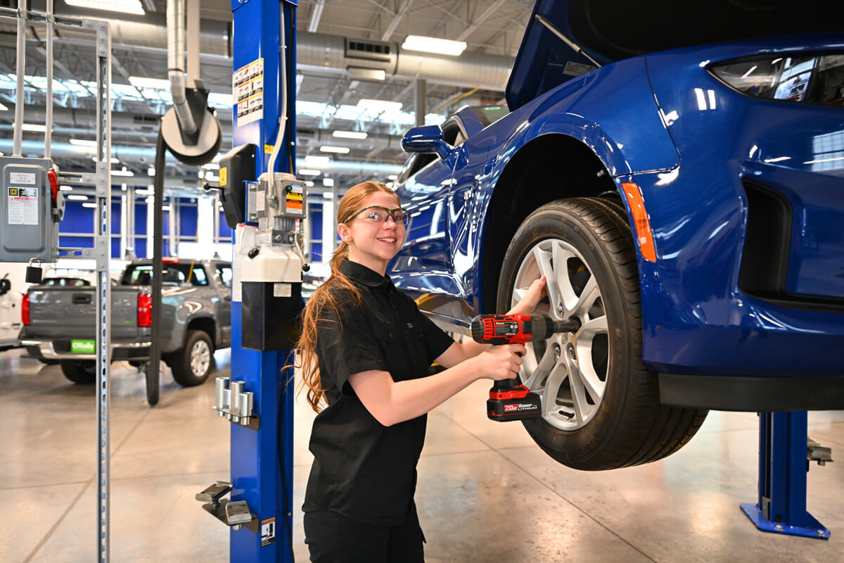 Jessa stands working on a vehicle while smiling at the camera