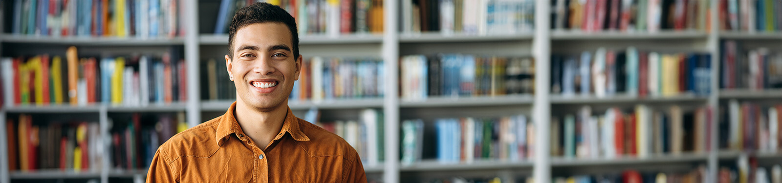 A male student stands smiling in a campus library