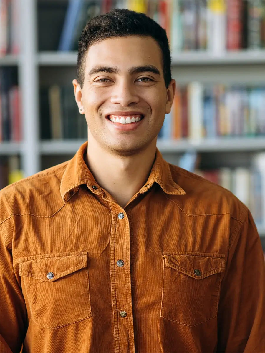 A male student stands smiling in a campus library