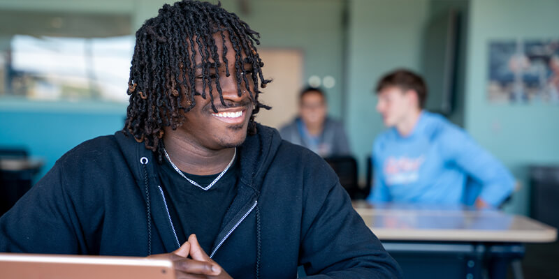 A male student smiles at a computer in a classroom 