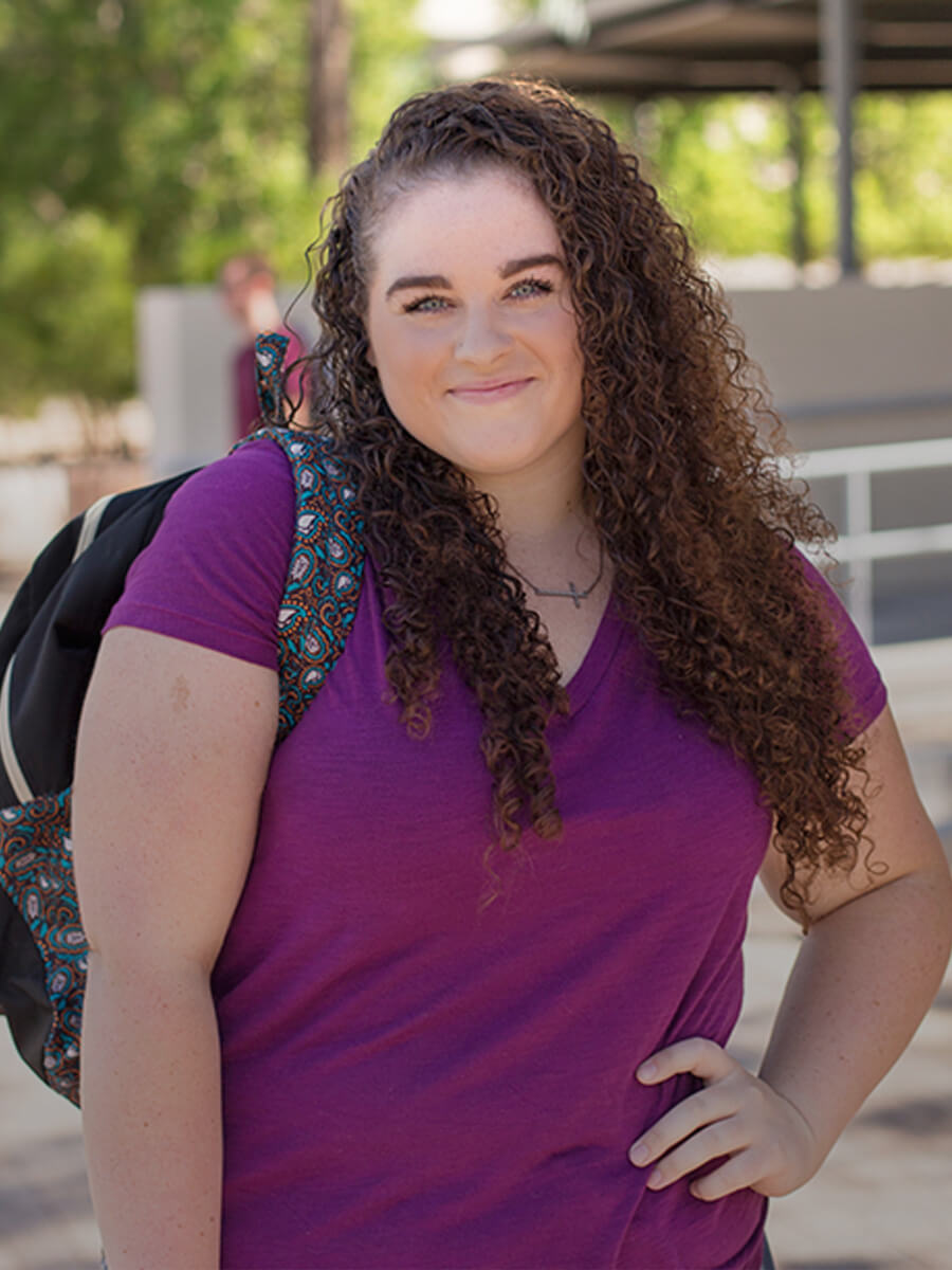 A female student stands smiling at the Downtown Campus Courtyard