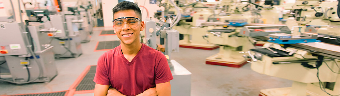 A student smiles in a warehouse with safety glasses on