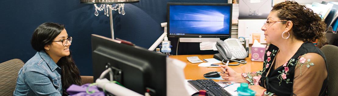 A human resources assistant works with a student at their desk in their office