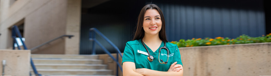 A medical assistant student smiles while wearing scrubs in a Pima West campus courtyard