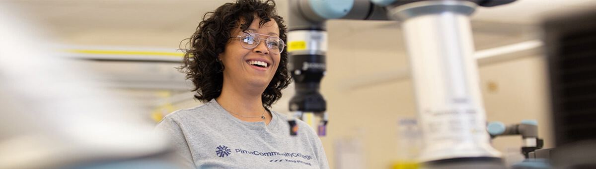 A student smiles while working on a manufacturing robot in Pima's AIT lab